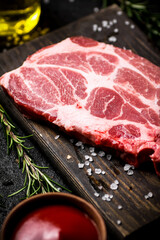 A steak of raw pork on a cutting board with tomato sauce and rosemary. 