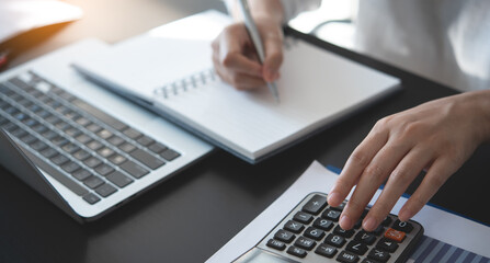 Businesswoman working at office, using calculator to calculate financial report, sales data, with laptop computer and business document on office table, close up. Business, finance and investment 