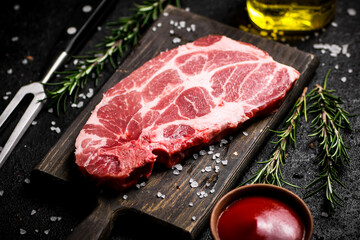 A steak of raw pork on a cutting board with tomato sauce and rosemary. 