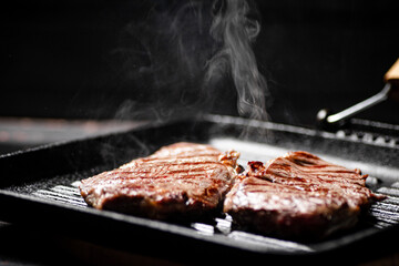 Cooking grilled steak in a frying pan with hot steam. 