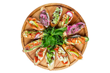 Assortment of bruschettas with different toppings served on a round wooden plate. Appetizing popular buffet snacks. Top view. Close-up. Isolated on white background.
