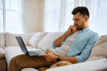 Pensive man reading an e-mail on laptop at home.