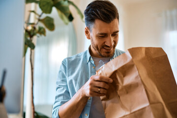 Happy man opening food delivery paper bag while working at home.