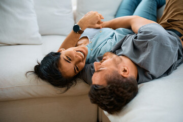 Happy couple talk while lying embraced on sofa at home.