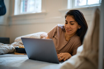 Happy woman surfing the net while relaxing on bed.