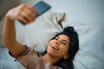 Cheerful woman has fun while taking selfie in bedroom.