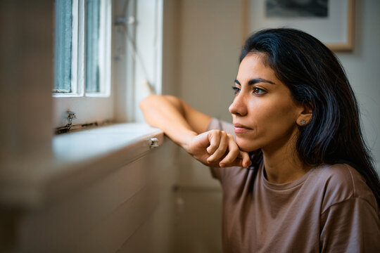 Pensive woman looking through window at home.
