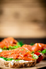Sandwich with salmon on a wooden background.