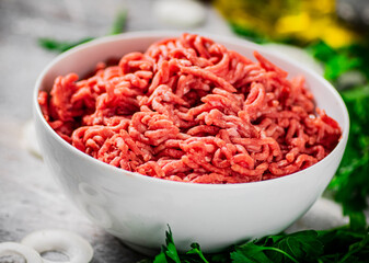 Minced meat in a bowl on a table with parsley and onion rings. 