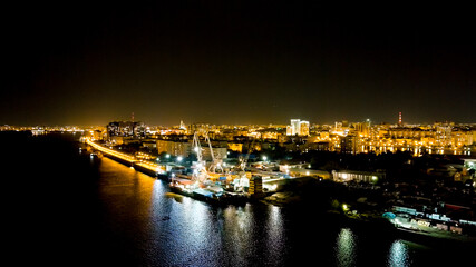 Astrakhan, Russia. Port cranes unload dry cargo. Working port. Embankment of the Volga River. Night city lights, Aerial View