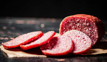 Sliced salami sausage on paper on the table.