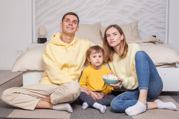Friendly family, cute parents with child boy son sitting by the bed and holding bowl with popcorn