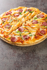 Americana pizza with french fries, sausages, cheese, base tomato sauce close-up on a wooden board on the table. Vertical
