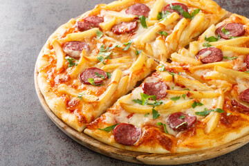Homemade pizza with french fries, wurstel, mozzarella cheese, tomato sauce and herbs close-up on a wooden board on the table. Horizontal