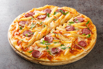 Tasty Americana Pizza with french fries, wurstel, cheese, tomato sauce and herbs close-up on a...
