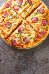 Americana pizza with french fries, sausages, cheese, base tomato sauce close-up on a wooden board on the table. Vertical top view from above