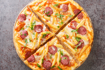 Homemade pizza with french fries, wurstel, mozzarella cheese, tomato sauce and herbs close-up on a wooden board on the table. Horizontal top view from above