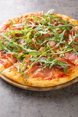 Pizza with prosciutto ham, cheese, tomato sauce and fresh arugula close-up on a wooden board on the table. Vertical
