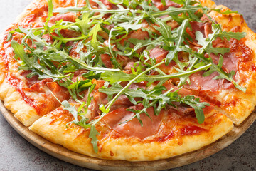 Pizza Prosciutto cooked with tomato sauce, mozzarella, ham, arugula, parmesan close-up on a wooden board on the table. Horizontal