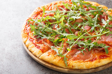 Classic Italian Pizza Prosciutto with tomato sauce, mozzarella, ham, arugula close-up on a wooden board on the table. Horizontal