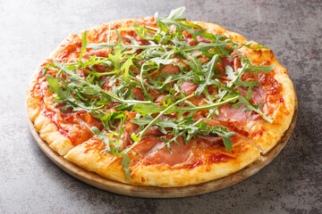 Hot pizza with prosciutto and arugula close-up on a wooden board on the table. Horizontal