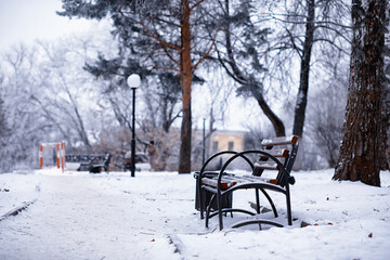 park bench on a winter alley at snowfall. bench with snow after snowstorm or in snow calamity in europe