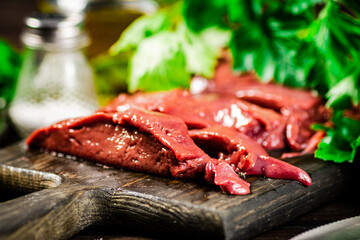 Pieces of raw liver on a cutting board with parsley and spices.