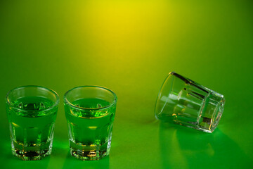 Two shot glasses lined up against emerald theme background filled with green spirit cocktail to be...