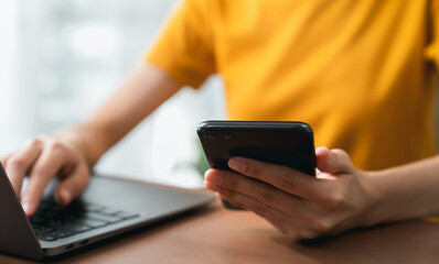 Hand holding smartphone and using laptop.