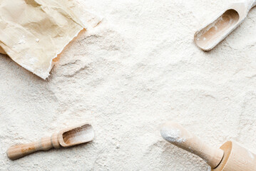 Background with flour. Rolling pin, wooden spoon, paper bag and flour, flat lay, top view.
