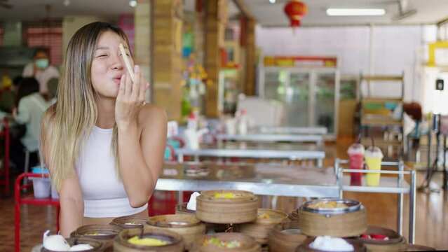 4K Portrait of Young Asian woman using chopsticks eating Chinese food steamed dumpling in bamboo steamer in Chinese restaurant. Attractive girl enjoy travel and eating street food on summer vacation.