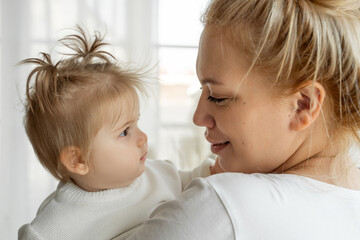 Mom Embrace Her Baby Toddler Girl Near Window At Home. Feeling Happiness, Adopt Family, Love And Care, Parenthood And Childhood.