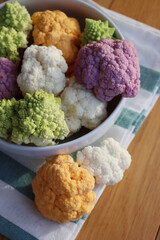 Various sort of cauliflower in a bowl on wooden table. Purple, yellow, white and green color cabbages and  green Romanesco or Roman cabbage