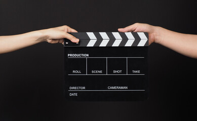 Two hands send and hold Black clapper board or movie slate on black background..