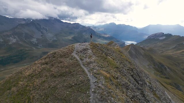 Aerial Epic Man standing on top of a mountain with panoramic view with mountains, lakes and clouds, Drone view, in the French Alps, France, Tour du Mont Blanc, near Refuge Croix du Bonhomme
