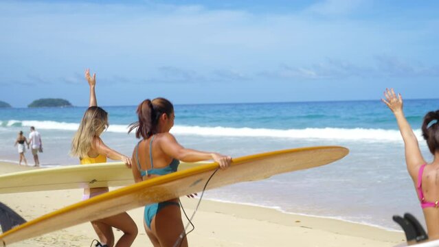 4K Group of Asian woman surfer in swimwear holding surfboard walking to the ocean on tropical beach in sunny day. Girl friends enjoy outdoor activity lifestyle water sport surfing on summer vacation.