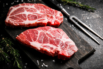 Raw pork steak on a cutting board with rosemary. 
