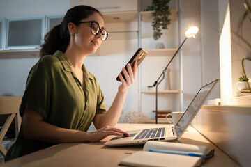 Caucasian smiling young woman using cellphone and working at laptop. Side view. Concept of remote...