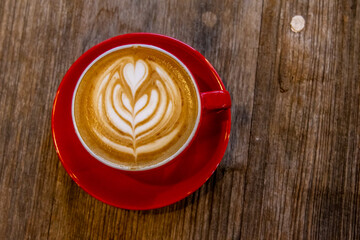 A red cup of coffee cappuccino with latte art on wooden background. Coffee house