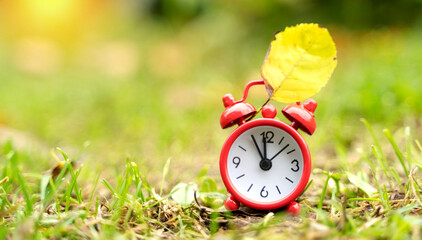 red alarm clock and yellow leaf on the grass, the concept of the end of summer