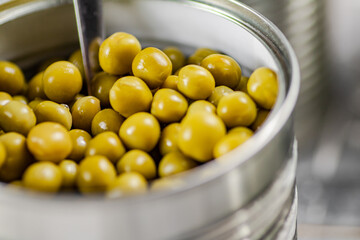 Open tin can with canned green peas with a spoon. 