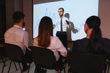 Man is standing near projector and showing graphs and business graphs.
