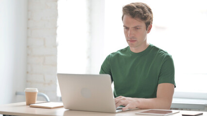 Fototapeta premium Busy Young Man Typing on Laptop in Office