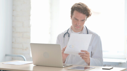 Young Doctor Working on Medical Report and Laptop in Clinic