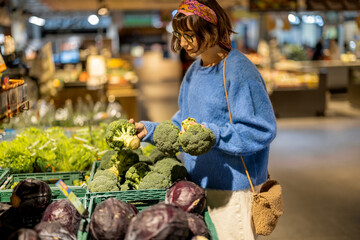 Young woman chooses broccoli, buying vegetables in supermarket. Concept of shopping groceries and...