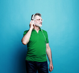 Senior bearded man listening to music with headphones over blue color background