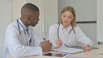 Female Doctor Discussing Medical Report with African Doctor, Paperwork