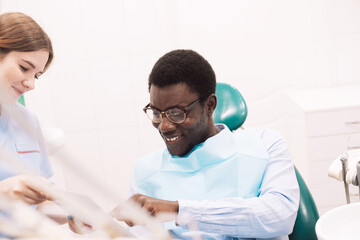 A young woman dentist makes a treatment plan for a black man. The doctor uses a tablet.