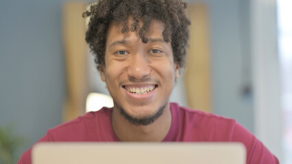 Fototapeta premium Close Up of African Man Smiling at Camera while using Laptop