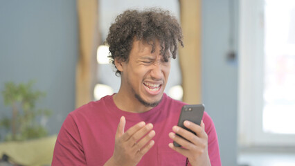 Fototapeta na wymiar Shocked African Man Reacting to Loss on Smartphone